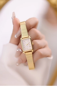 Close-up of golden rectangular quartz watch with Roman numerals and elastic metal band