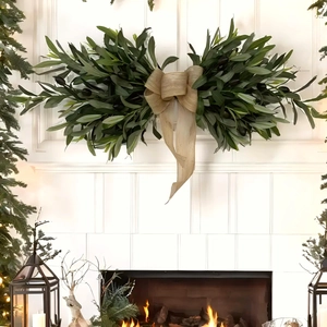 Artificial olive leaf wall swag with burlap bow hanging over a cozy fireplace