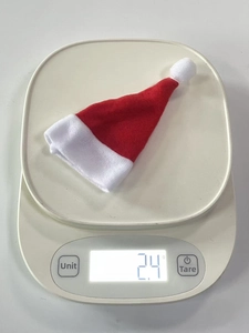Detailed view of a mini red Christmas hat on a digital scale weighing exactly 2.4 grams