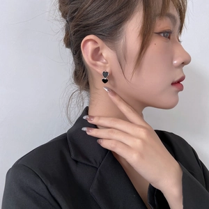 Detail view of double black heart earrings on a female model wearing a black blazer