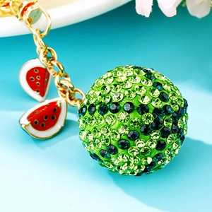 Close-up of sparkling rhinestone watermelon keychain with gold metal hardware on blue base