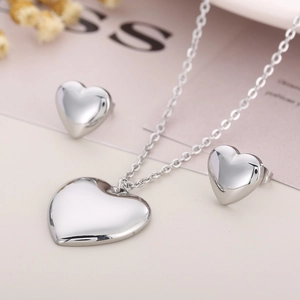 Polished silver heart-shaped necklace and earring jewelry set shown with dried flowers