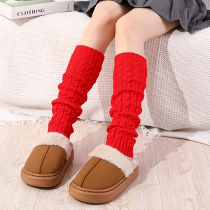 Close-up of red cable knit leg warmers paired with plush slippers in a cozy room