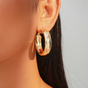 Close-up of model wearing thick gold hoop earrings with a polished metallic finish