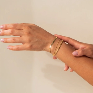 Gros plan d'un ensemble de bracelets gourmettes et perles dorés superposés sur le poignet