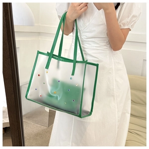 Detailed shot of large transparent PVC tote bag with green trim and color rivets on a model