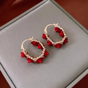 Boucles d'oreilles en U dorées avec fleurs rouges et strass sur boîte à bijoux