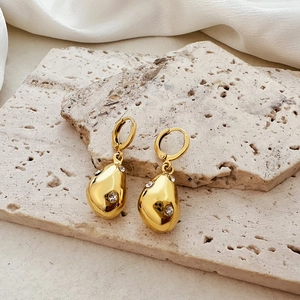 Elegant gold teardrop earrings with zircon stone on a beige stone and silk background
