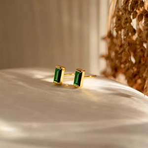 Macro shot of gold-plated rectangle emerald studs featuring step-cut green crystals