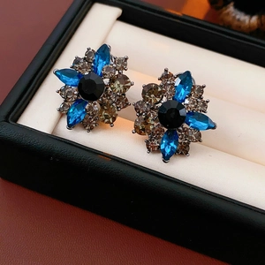 Dettaglio di orecchini vintage a fiore con cristalli blu e grigi su cuscinetto nero