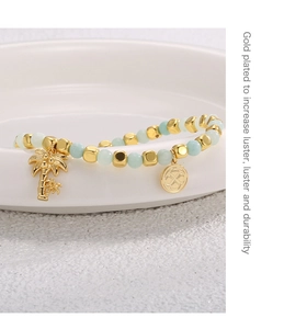 Detail of gold-plated palm tree bracelet with green beads on a white ceramic plate