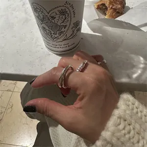 Detail of silver twisted rope and double-cross rings worn on hand in a cafe setting