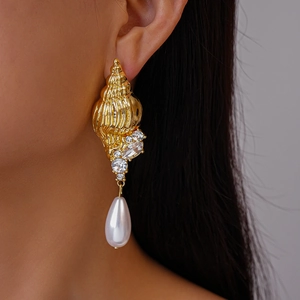 Golden conch shell earrings with water drop pearls and crystal accents on female model