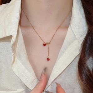 Macro shot of gold Y-chain necklace featuring red enamel heart charms on a model