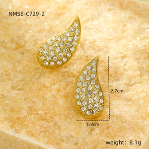 Macro shot of gold teardrop earrings with white zircon on stone background