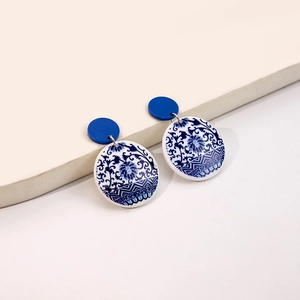 Detail of round blue and white porcelain pattern earrings on minimalist white background