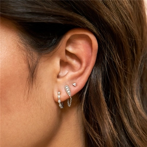 Detailed macro view of silver earring set featuring studs, teardrop chain, and textured hoops