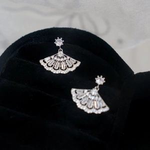 Macro shot of fan-shaped silver earrings with sparkling zircon inlay on black jewelry box