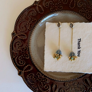 Detail of vintage gold earrings with blue enamel bell shapes and green bead fringe