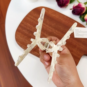 Large cream acetate shark hair claw clip shown in hand with elegant floral background