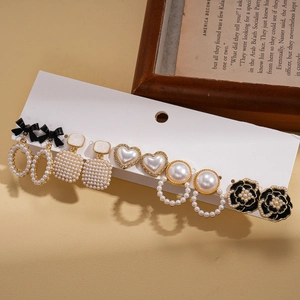 Elegant 6-pair gold earring set with faux pearls, black enamel flowers, and bows on display