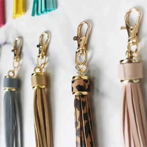 Colorful leather tassel keychains with gold metal rings displayed on marble surface
