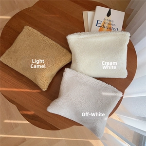 Three plush faux shearling makeup bags in camel, cream, and off-white on a wooden table