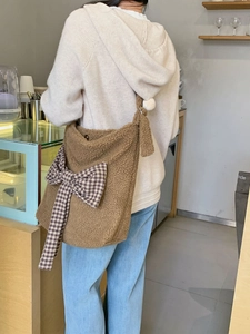 Detailed close-up of brown plush crossbody bag with houndstooth bow in a cozy cafe setting