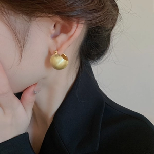 Detail of matte gold sphere earrings on model showing brushed metallic texture