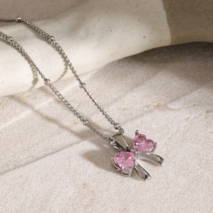 Macro detail of silver bow pendant with pink heart-shaped zircons on beaded chain necklace