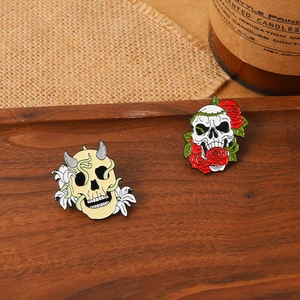 Detailed close-up of gothic skull enamel pins with lily and rose on vintage wood background