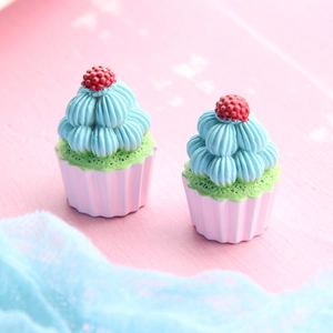 Close-up of miniature resin cupcakes with green frosting and red berries on pink wood
