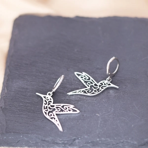 Close-up of hummingbird earrings with detailed cutout patterns on a black stone slab