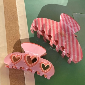 Detailed view of pink heart cutout and striped acrylic hair claws with a glossy finish
