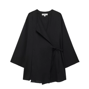 Detail of black wrap top with side tie closure and woven fabric texture on white background