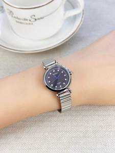 Close-up of a silver metal watch with diamond indexes and blue hands on a female wrist