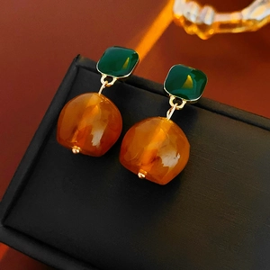Detail of geometric earrings featuring square green stones and orange resin pendants