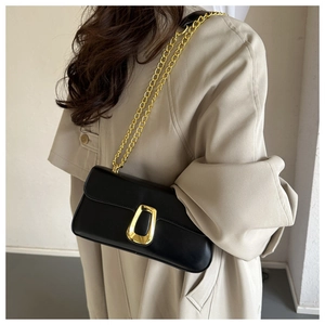 Detail of a black leather crossbody bag with a gold buckle worn with a beige trench coat