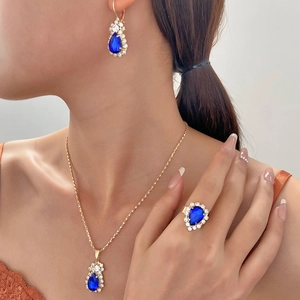 Detailed view of model wearing gold waterdrop blue sapphire necklace, earrings and ring set