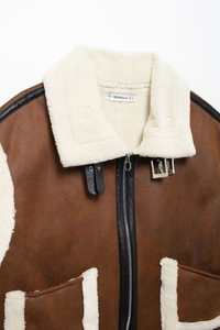 Close-up of brown faux suede vest with cream faux fur lining and buckle collar detail