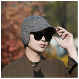 Detail of grey winter knit beanie with ear flaps and brim worn by male model outdoors