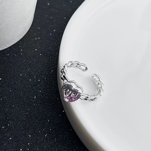 Close-up of heart-shaped purple zircon ring with silver chain band on a ceramic plate