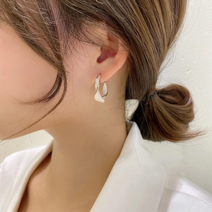 Close-up of twisted gold metal hoop earring with white enamel inlay on female model