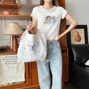 Détail du sac en toile blanche avec broderie papillon colorée et bordure orange vif