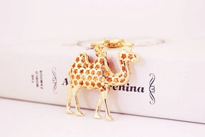Close-up of golden camel keychain with rhinestone details on a soft pink background