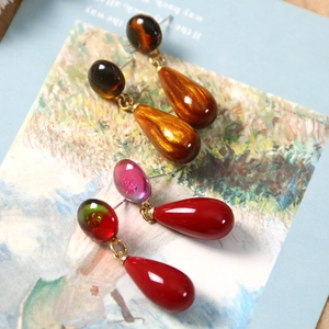 Macro detail of glossy colorful resin teardrop earrings on an artistic postcard background
