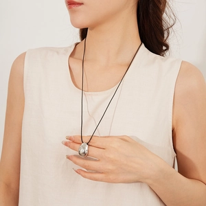 Gros plan d'un collier pendentif goutte d'argent minimaliste sur un cordon de cire noir