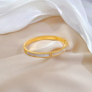 Detail of gold titanium steel bangle with shell inlay and three centered cubic zirconia