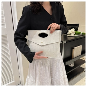 Detail of white crocodile pattern tote bag with oval cutout handle and gold snap button