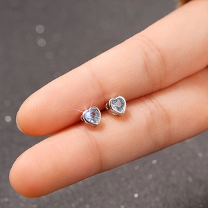 Macro shot of light blue heart-shaped silver earrings held by hand to show compact size